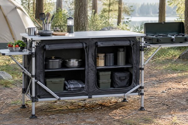 A foldable camping kitchen station with an aluminum worktop and organized fabric storage set up beside a tent at a quiet campsite.